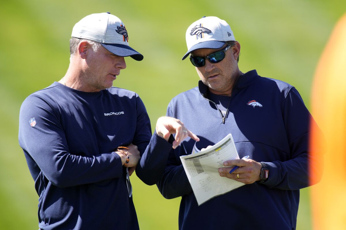 FILE - Denver Broncos offensive coordinator Pat Shurmur, left, confers with quarterbacks coach Mike Shula during NFL football practice on Sept. 16, 2021, at the team's headquarters in Englewood, Colo. The Broncos are making backup play-calling plans after ] Shurmur tested positive for the coronavirus Friday, Nov. 12, 2021, and went on the reserve/COVID-19 list. Prime candidates are quarterbacks coach Mike Shula, who will communicate with QB Teddy Bridgewater through his headset, or O-line coach Mike Munchak. (AP Photo/David Zalubowski, File)