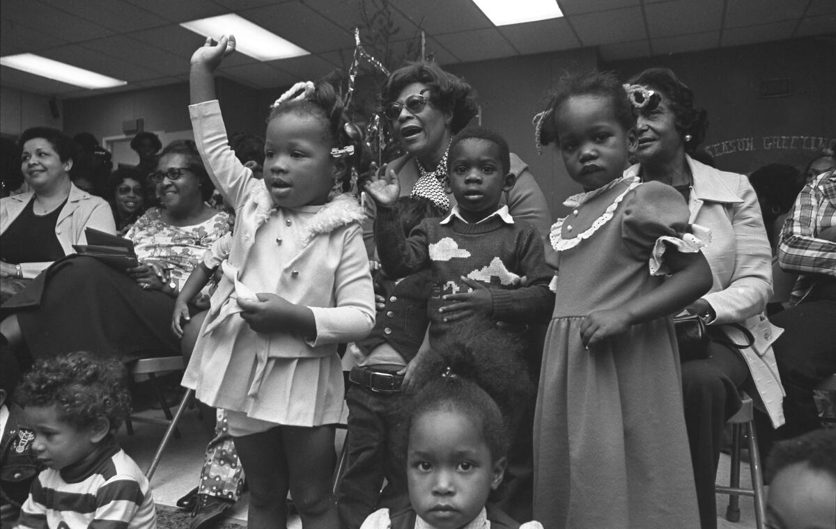 A woman surrounded by young children sings.
