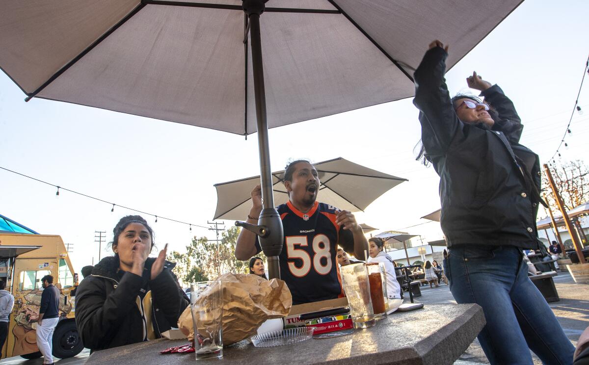 Three people cheer at an outdoor table.