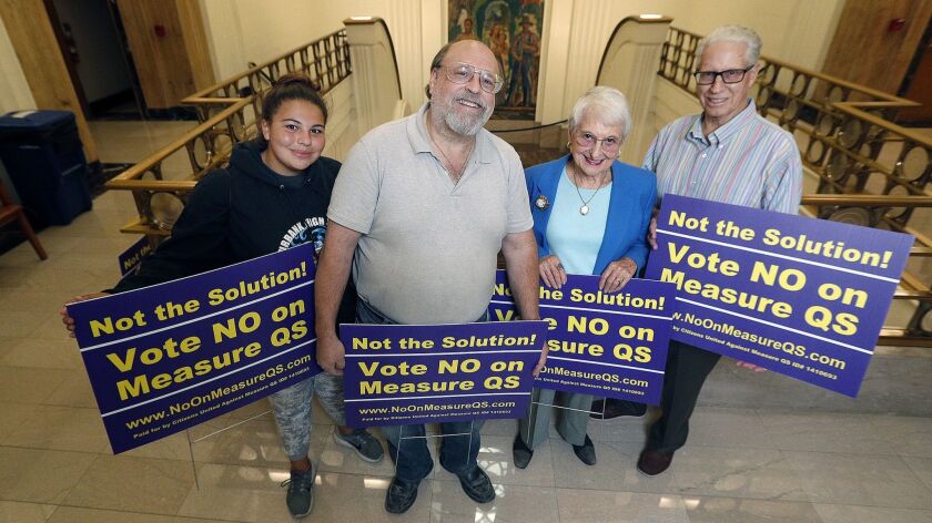 Lauren Applebaum, 16, Larry Applebaum, Audrey Hanson, and Bill Abbey hold No on Measure QS signs inside Burbank City Hall before the latest Burbank Unified board meeting. Larry Applebaum authored the voter guide argument against Measure QS co-sponsored by Hanson and Abbey.