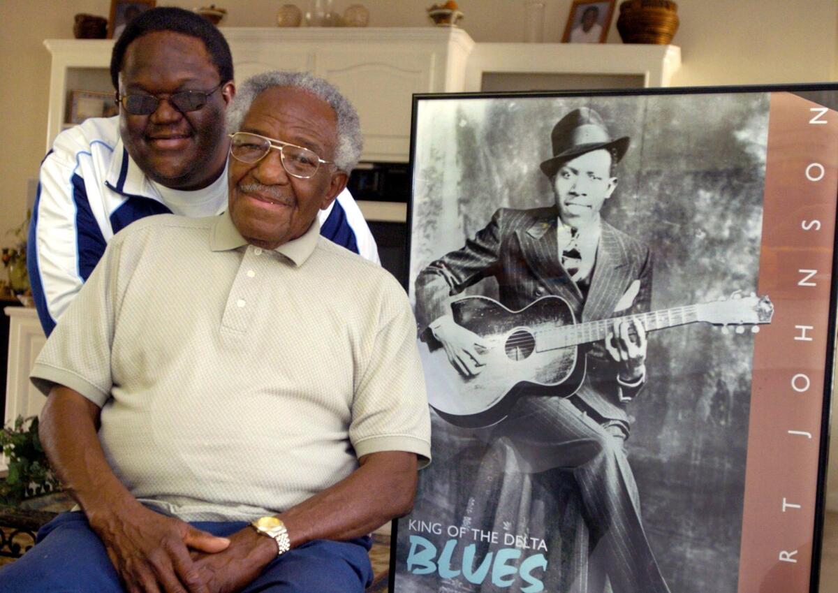 Claud Johnson, seated, son of legendary Mississippi blues artist Robert Johnson, shown in the poster on the right, has died at age 83. Johnson is shown with his son Michael Johnson.