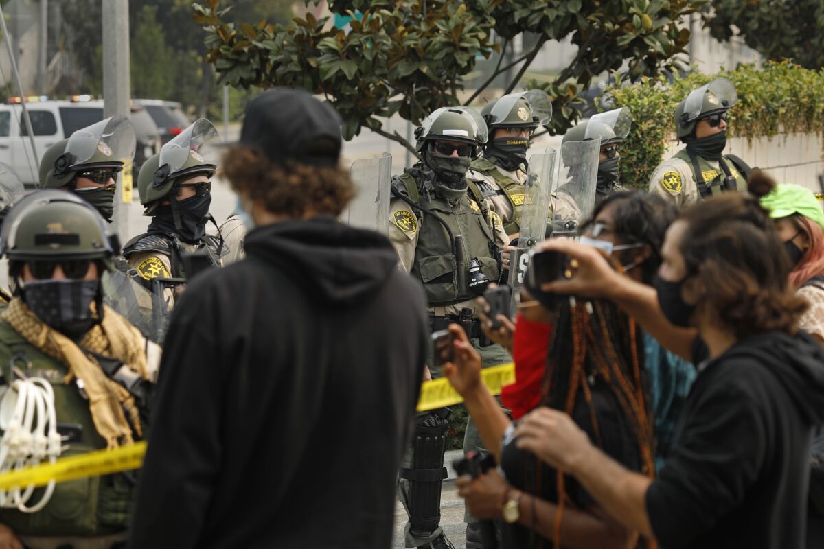 Los Angeles County sheriff's deputies in riot gear watch as protesters hold a news conference in South L.A.