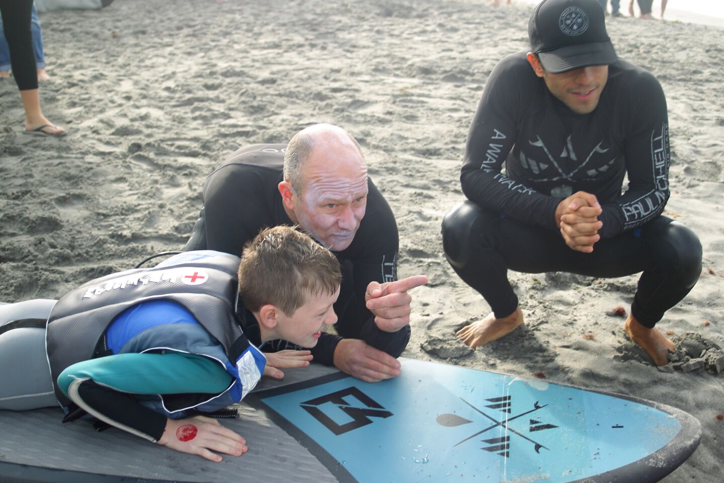 Mike Miller and Raphael Lopez help Brandon practice on shore before going into the water
