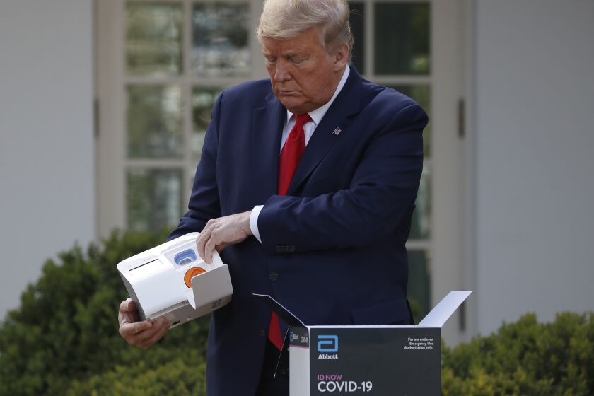 President Donald Trump opens a box containing a 5-minute test for COVID-19 from Abbott Laboratories as Stephen Hahn, commissioner of the U.S. Food and Drug Administration, speaks about the coronavirus in the Rose Garden of the White House, Monday, March 30, 2020, in Washington. (AP Photo/Alex Brandon)