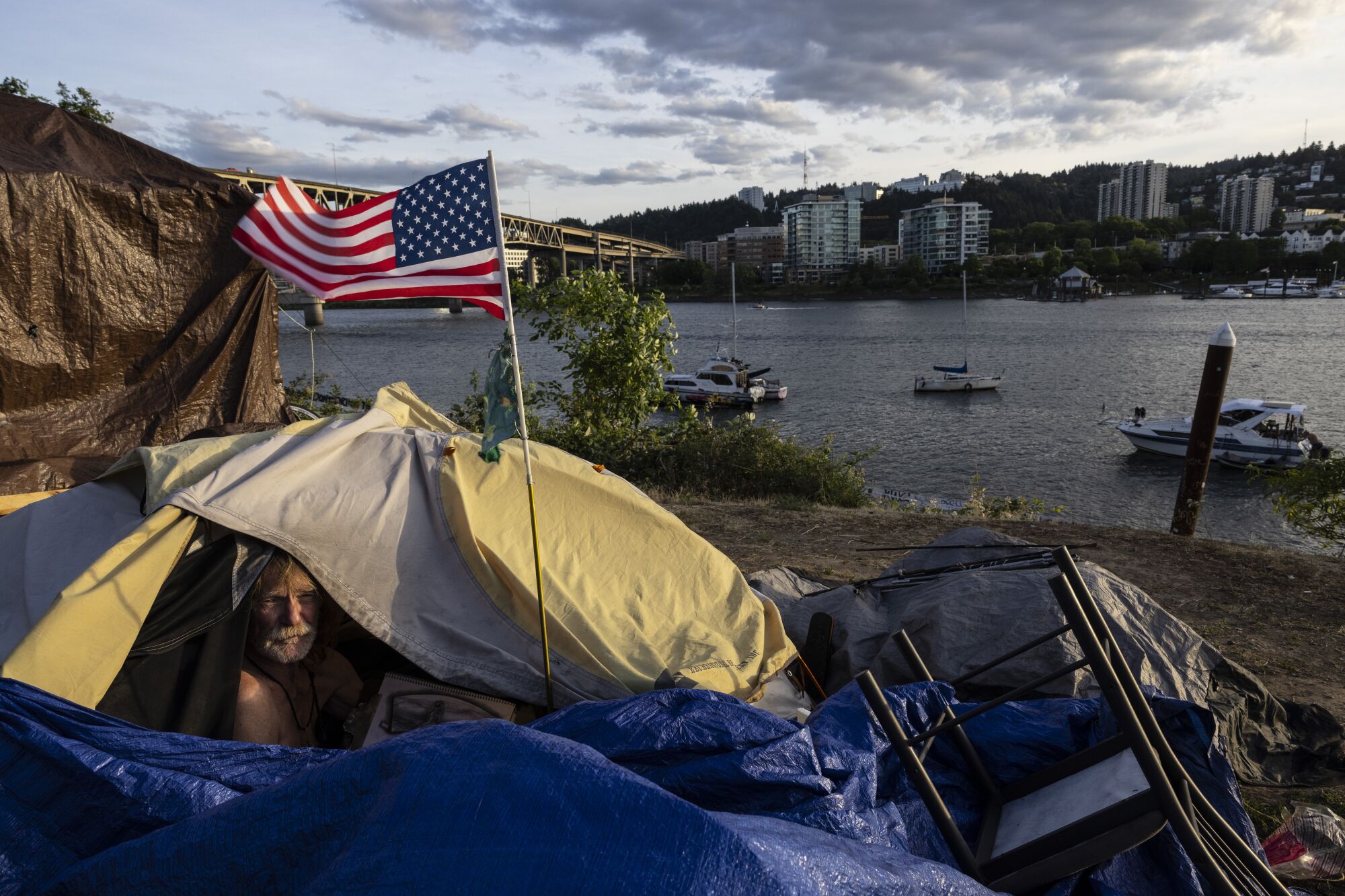 A man sits in a tent next to a river in Portland, Ore.