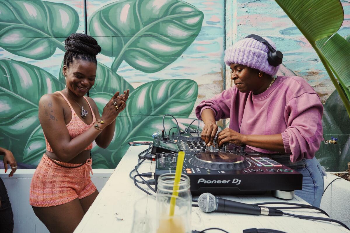 A Black woman dances at the DJ table while another Black person DJs