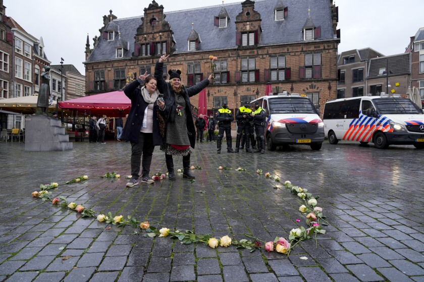 Dos mujeres posan luego de colocar unas rosas en forma de corazón mientras la policía vigila el centro de la ciudad de Nimega, Holanda, luego de que se prohibió la realización de una protesta contra las restricciones de COVID-19, el domingo 28 de noviembre de 2021. (AP Foto/Peter Dejong)