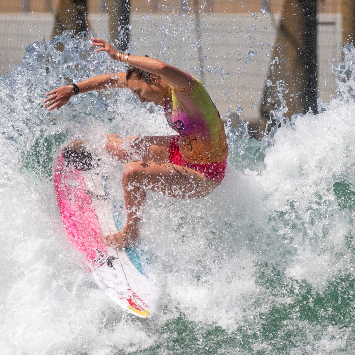 A woman on a pink, white and blue surfboard rides the waves.