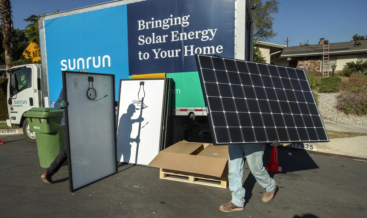 A person lifts a solar panel in front of a Sunrun truck.