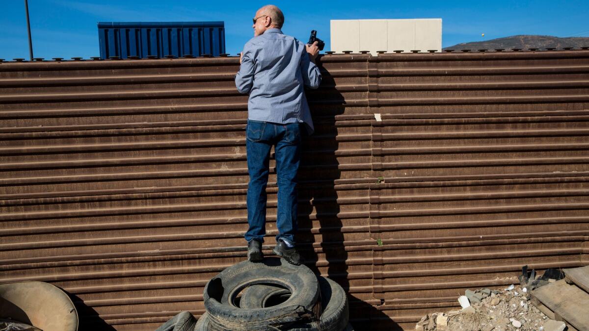 John Thurston peers over the existing U.S.-Mexico border wall to see the prototypes on a tour arranged by artist Christoph Büchel.