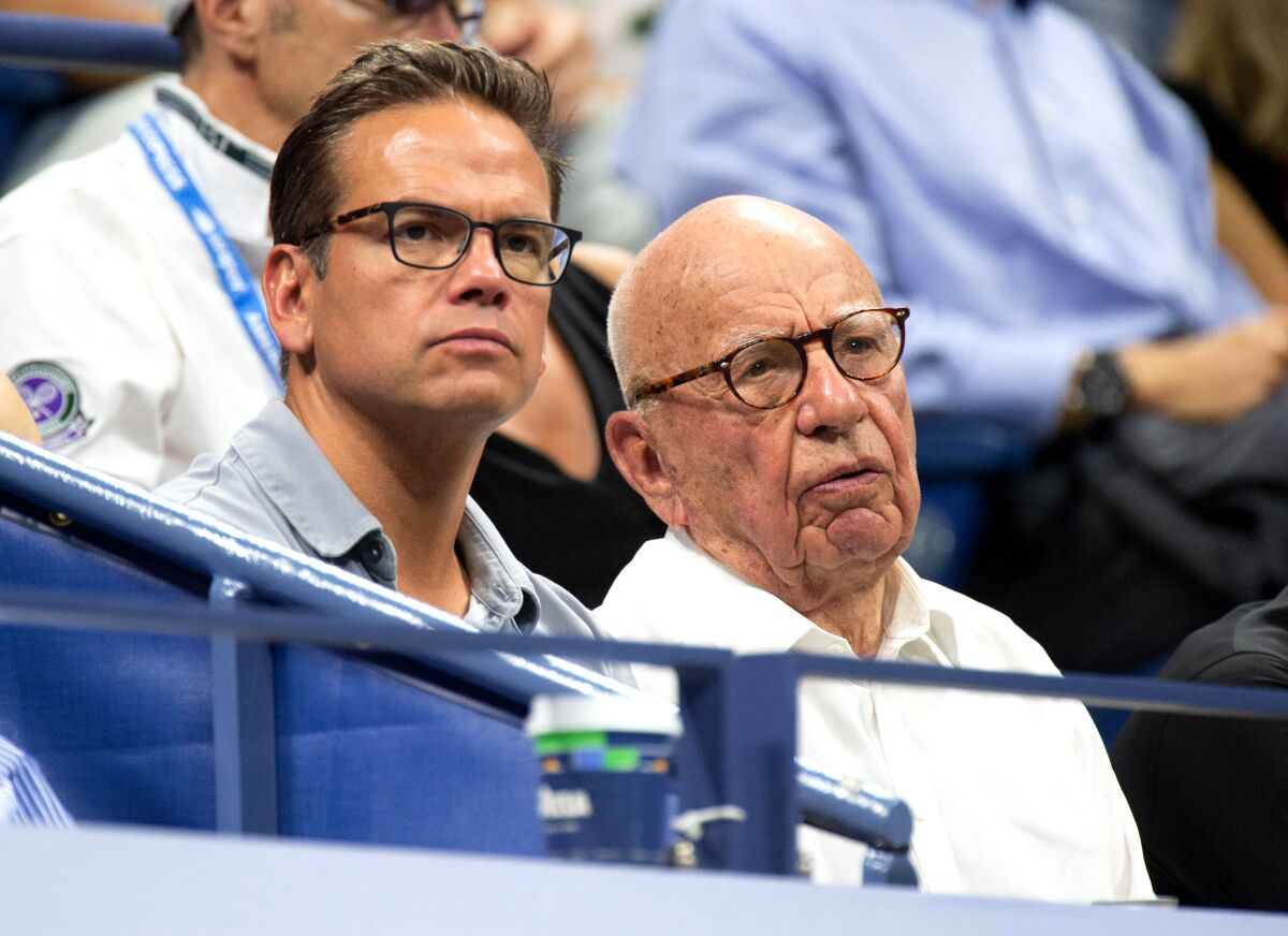 A younger and older man, both wearing glasses, sit in the stands of the U.S. Open tennis tournament.