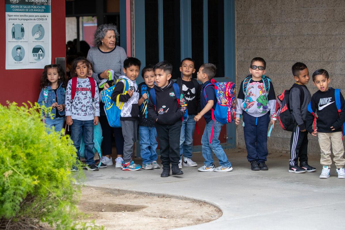 Transitional kindergarten children stand with their teacher outside of school.   