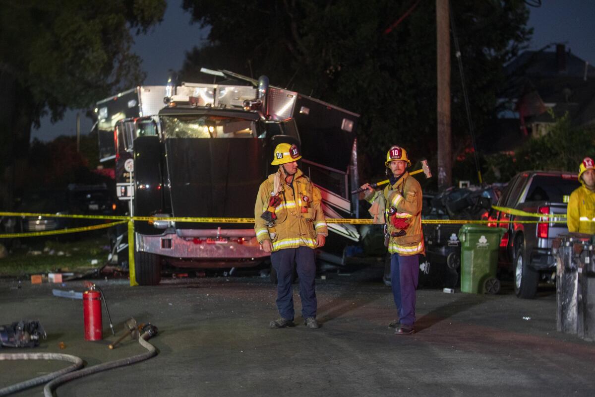 Two firefighters stand near the wreckage of a bomb squad truck.