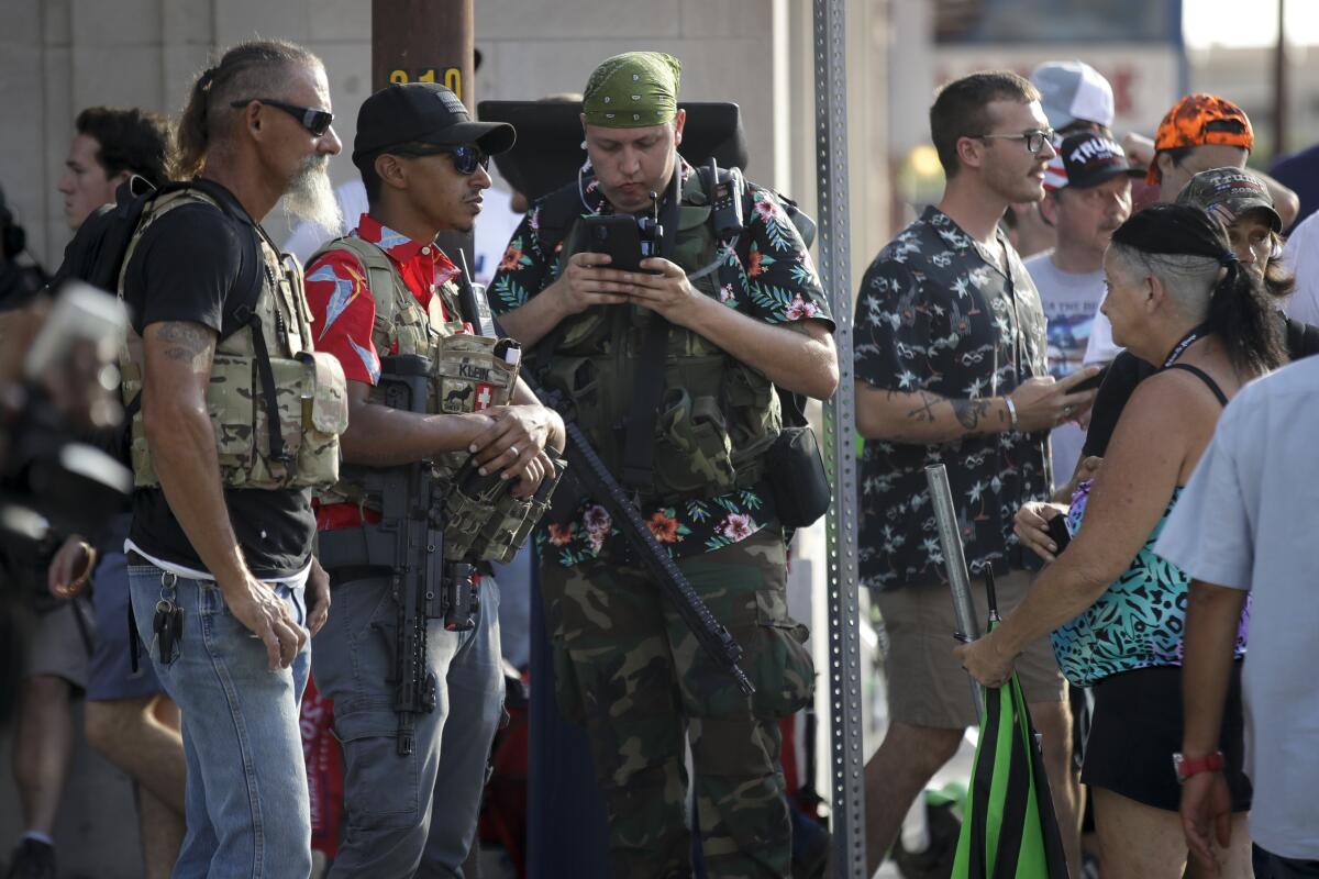 FILE - In this June 20, 2020 file photo, gun-carrying men wearing Hawaiian print shirts associated with the boogaloo movement watch a demonstration near where President Trump had a campaign rally in Tulsa, Okla. People following the anti-government boogaloo movement, which promotes violence and a second U.S. civil war, have been showing up at protests across the nation armed and wearing tactical gear. But the movement has also adopted an unlikely public and online symbol: Hawaiian print shirts. (AP Photo/Charlie Riedel, File)