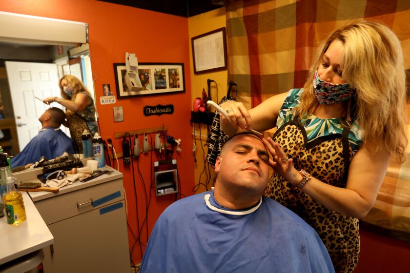 ATWATER, CA - MAY 26, 2020 - - Rosa Pedraza, wearing a protective mask against COVID-19, cuts Robert Nunez' hair at Rosa Hair Salon in Atwater, California on May 26, 2020. Pedraza has owned the business for 17 years in Atwater. California Governor Gavin Newsom says California counties that have been granted regional variances allowing more types of businesses to reopen can now permit the reopening of barbershops and hair salons, with modifications such as protective gear and face coverings. (Genaro Molina / Los Angeles Times)