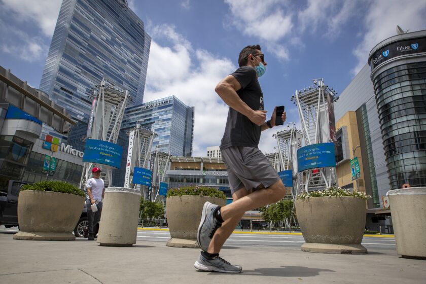 LOS ANGELES, CA - JUNE 18: A jogger wears a protective mask to protect from contracting COVID-19 while passing L.A. LIVE Thursday, June 18, 2020 in Los Angeles, CA. Gov. Gavin Newsom on Thursday ordered all Californians to wear face coverings while in public or high-risk settings, including when shopping, taking public transit or seeking medical care, following growing concerns that an increase in coronavirus cases has been caused by residents failing to voluntarily take that precaution. (Allen J. Schaben / Los Angeles Times)