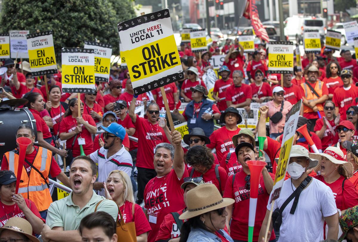 A crowd of hotel workers protest holding signs that say "on strike"