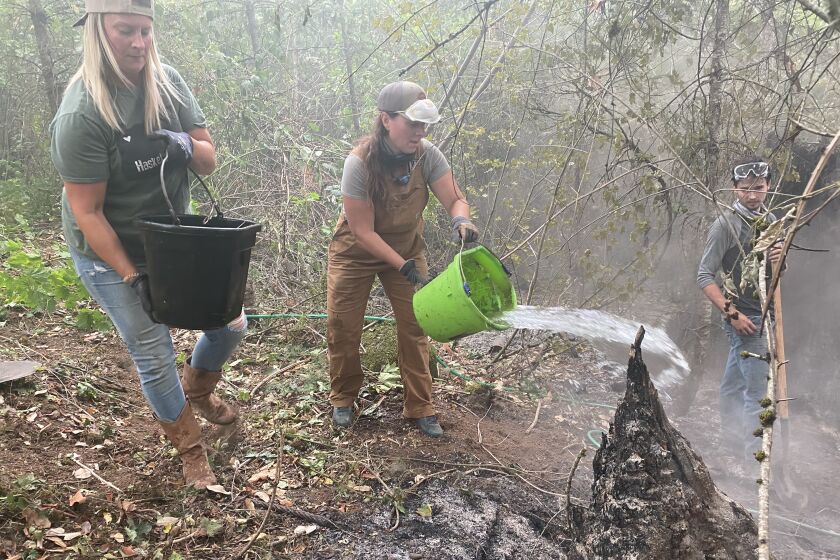 Amid a shortage of firefighters, Christine VanOeveren, right, throws water on a hotspot on a fire line near Molalla, Ore., as Melissa Rose prepares another bucket load.