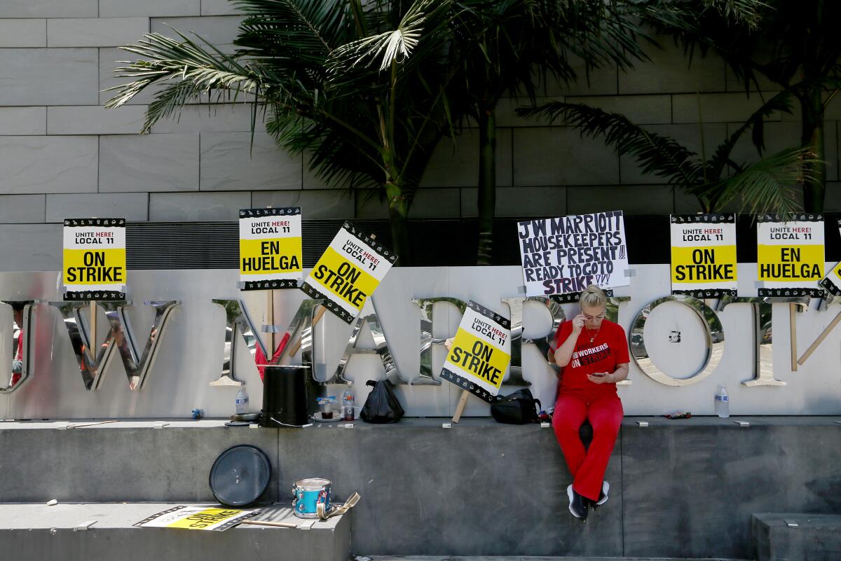 A picketer sits on a ledge outside the JW Marriott hotel in downtown L.A. on Monday, flanked by picket signs.