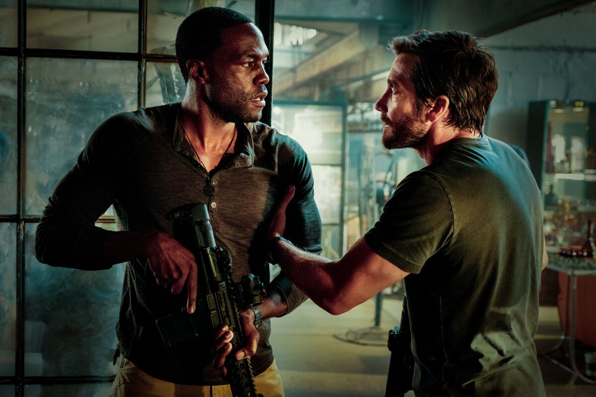 A man grabs the arm of another man holding a rifle in the movie “Ambulance”