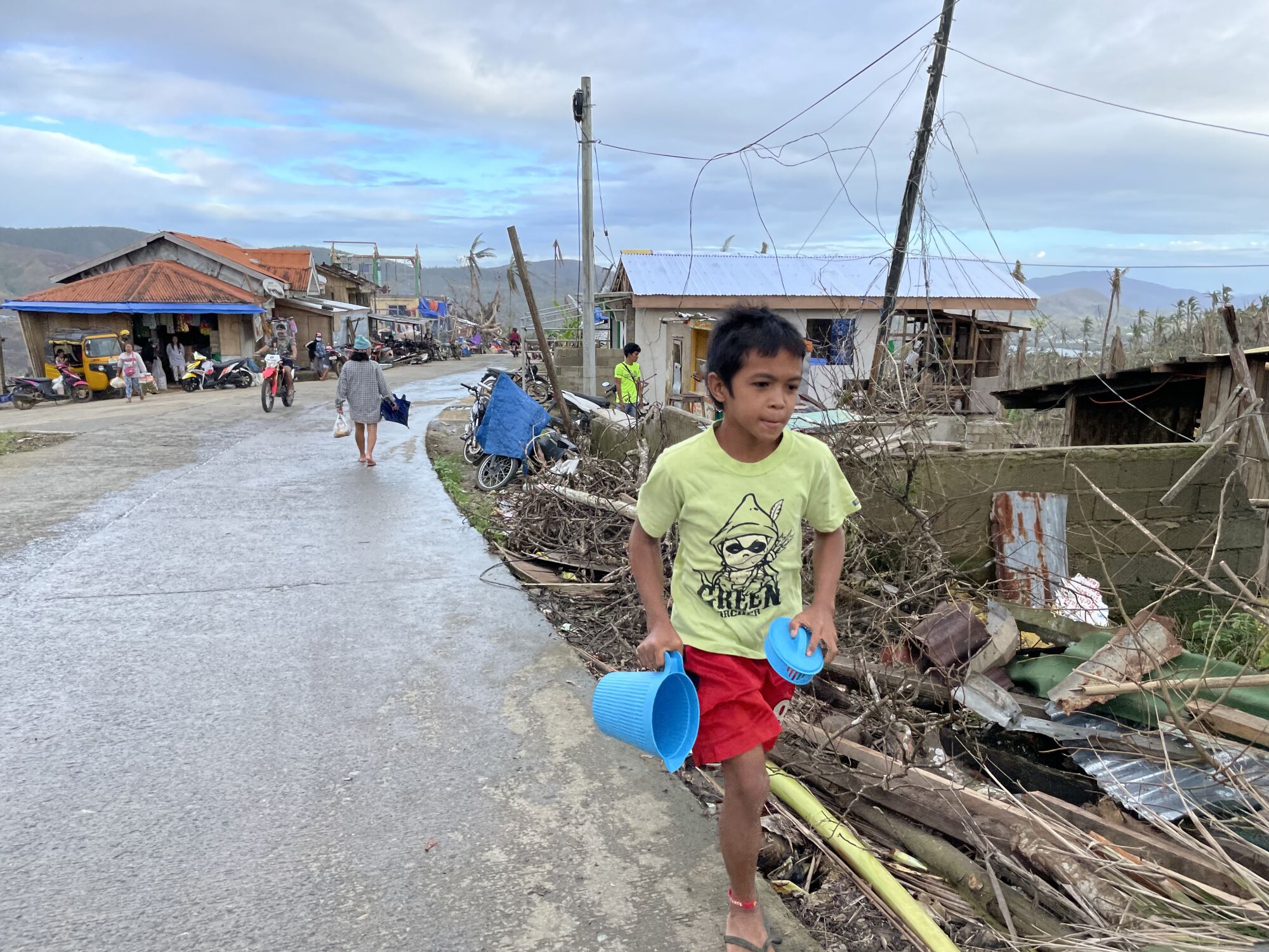 A boy walks down a street with debris next to it.