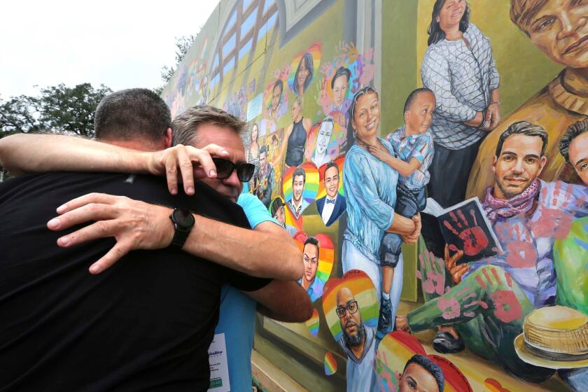 Artist Yuriy Karabash hugs a family member of a victim at the Pulse nightclub, Monday, June 12, 2017, in front of his mural that commemorates the one-year anniversary of the June 12, 2016, massacre that killed 49 at Pulse. (Joe Burbank /Orlando Sentinel via AP)