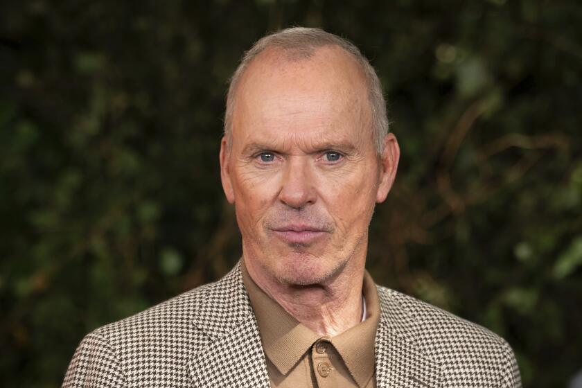 Michael Keaton poses for photographers in a tan polo and brown houndstooth blazer