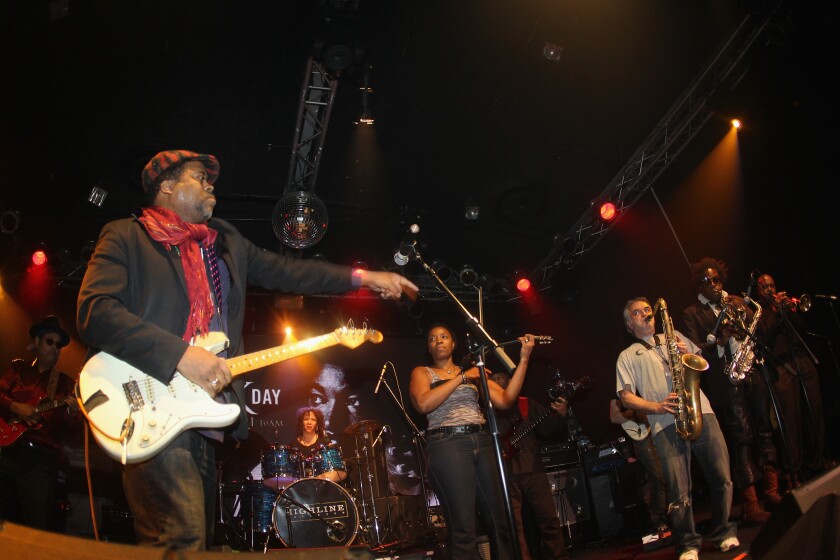 A band on stage, with a guitarist, a drummer and a brass section.