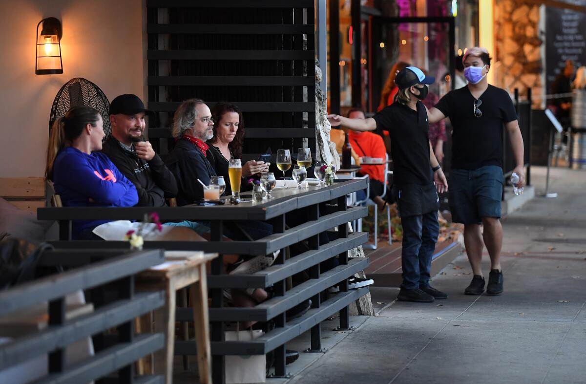 People eat on a sidewalk-facing patio outside a restaurant