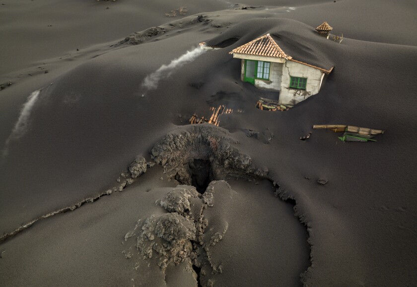 FILE - A fissure is seen next to a house covered with ash on the Canary island of La Palma, Spain, Dec. 1 2021. A volcanic eruption in Spain’s Canary Islands shows no sign of ending after 85 days. It became the island of La Palma’s longest eruption on record on Sunday, Dec. 12. (AP Photo/Emilio Morenatti, file)