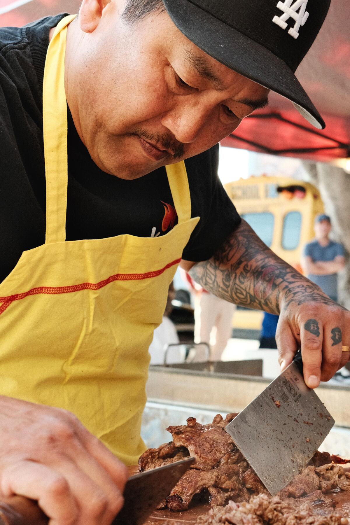 Kogi founder Roy Choi, in a yellow apron and L.A. baseball hat, prepares al pastor