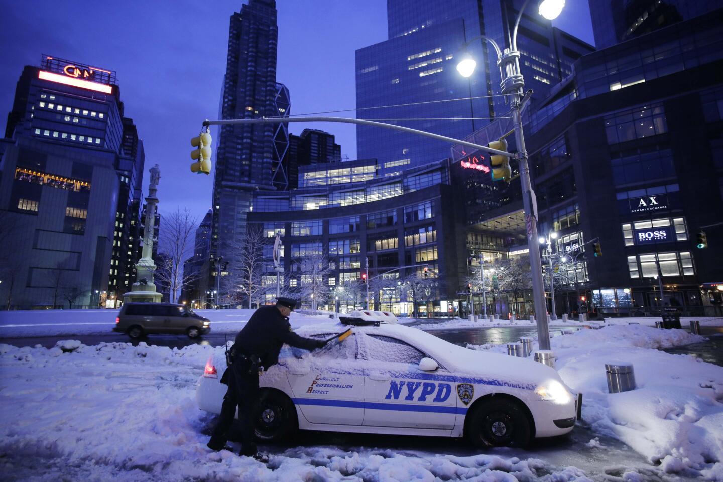 A New York City police officer clears snow from his car.