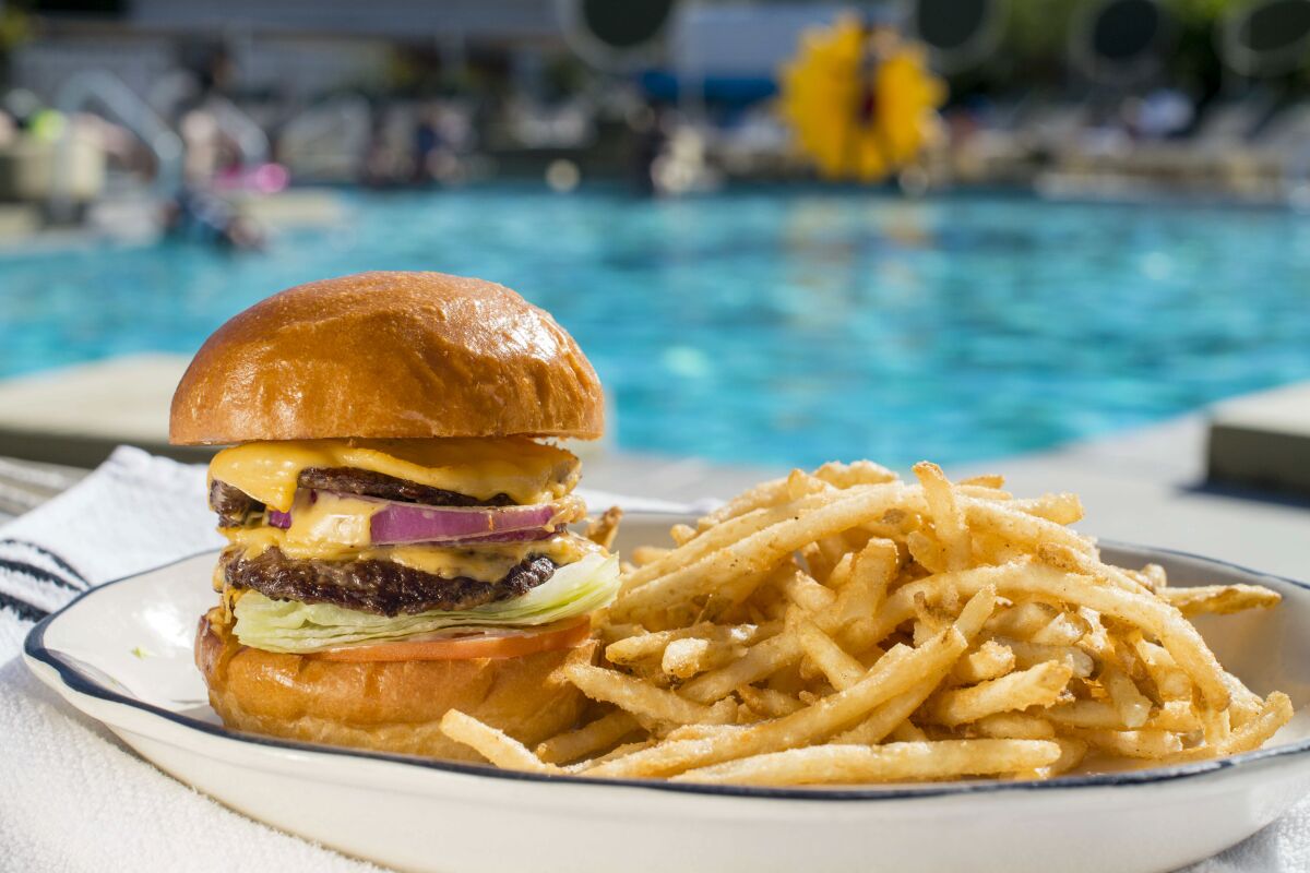 A burger and fries on a plate with a swimming pool in the background