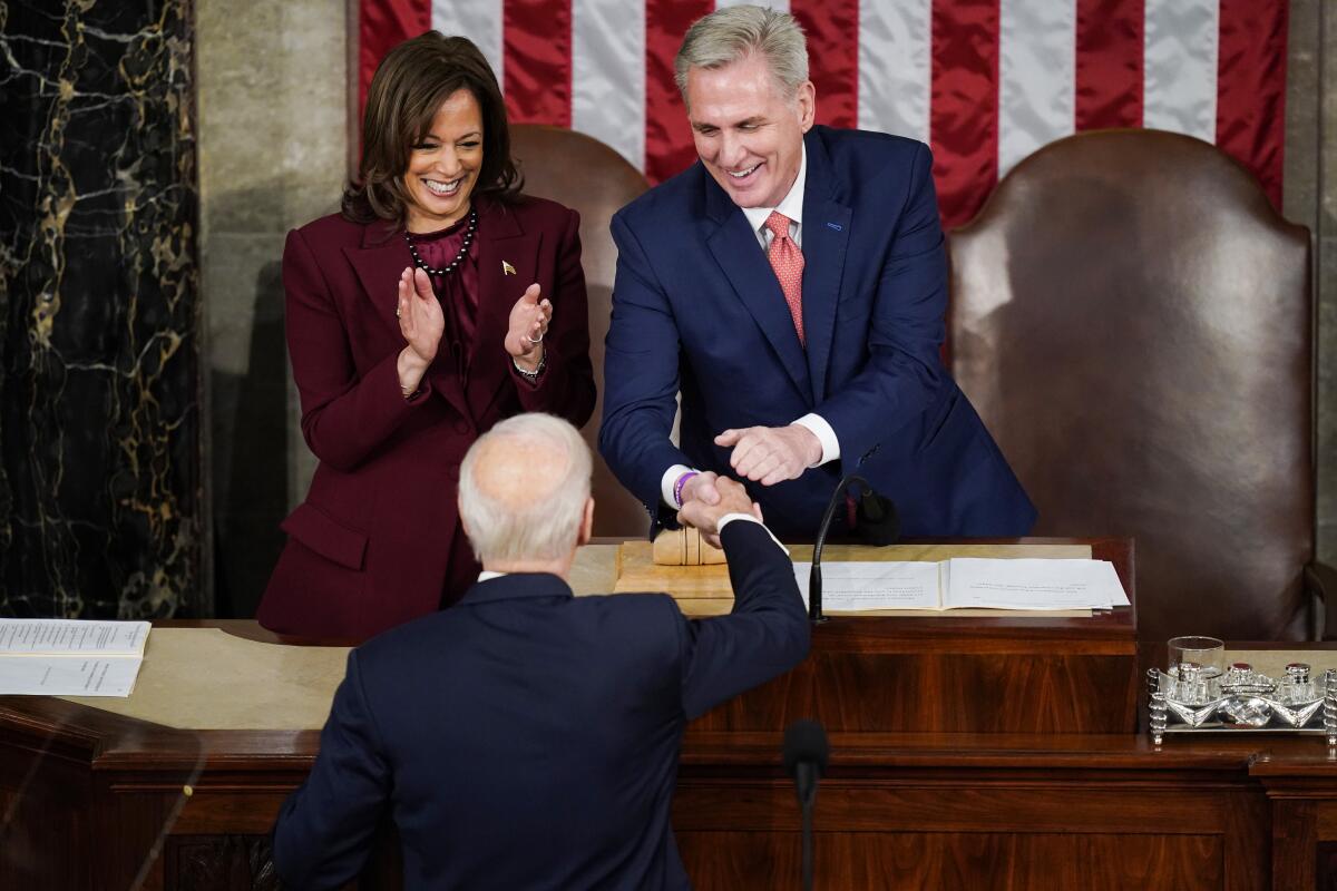 President Biden reaching up to shake hands with Speaker Kevin McCarthy as Vice President Kamala Harris claps