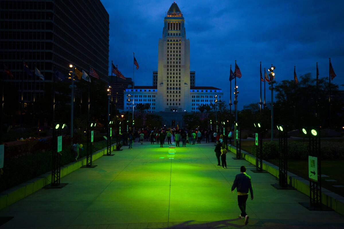 Los Angeles City Hall against a darkening sky, with a green-lighted walkway leading toward it.