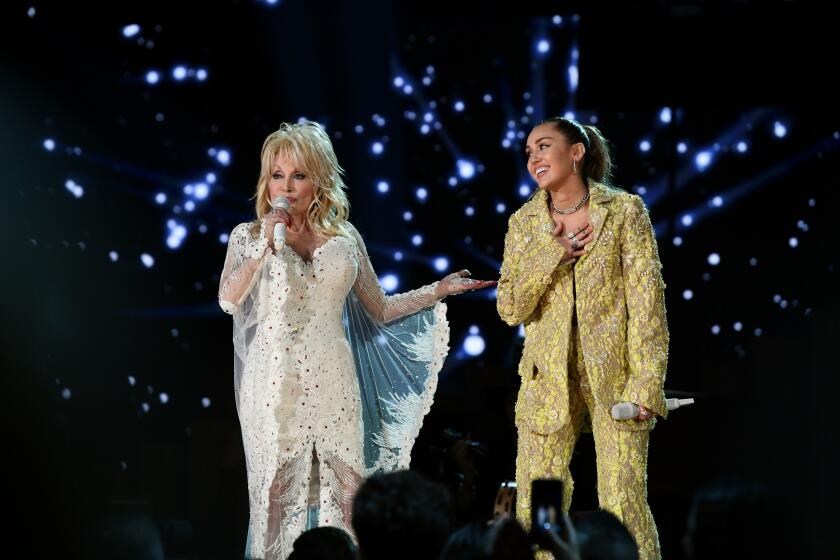 Dolly Parton in a white gown singing alongside Miley Cyrus in a gold oversized suit at the 61st Annual Grammy Awards.