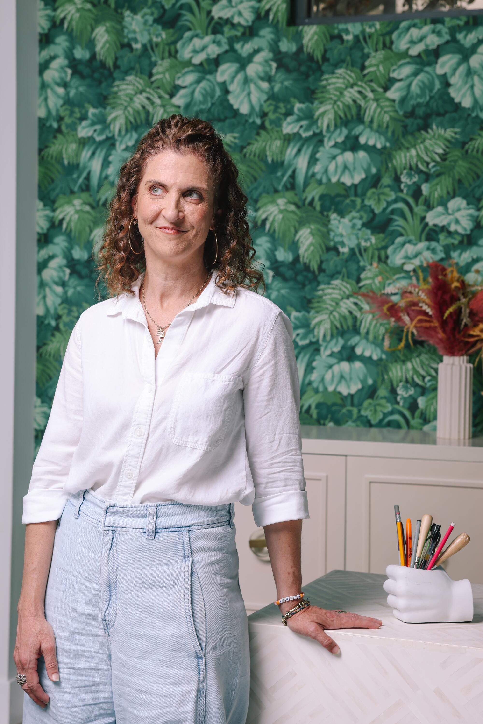 A woman with curly hair leans on a desk. 