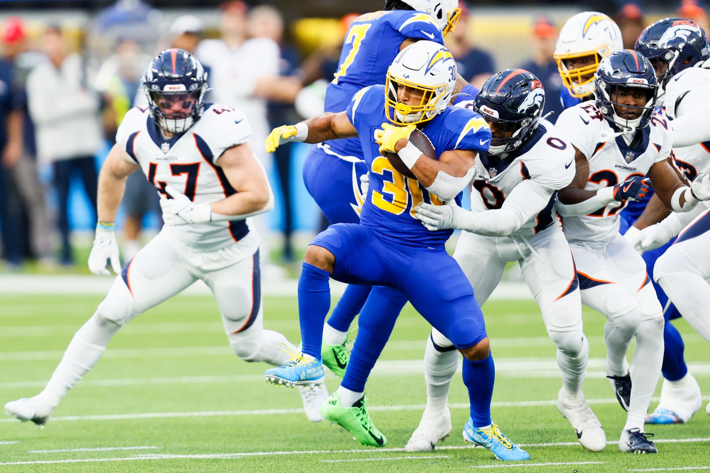 Chargers running back Austin Ekeler tries to evade tackle attempts by Denver defenders during a game last season.