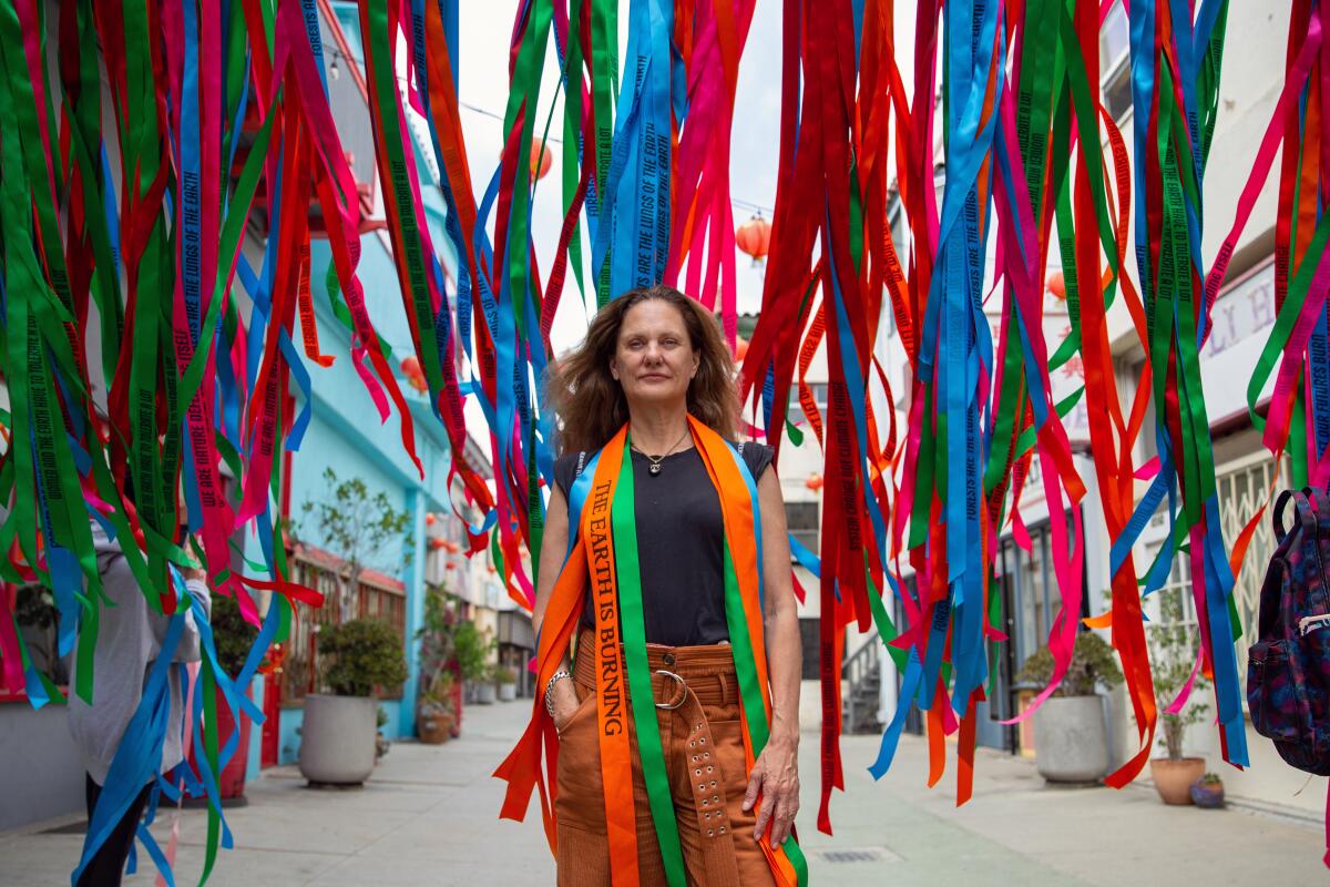 A woman stands amid an array of floating ribbons. She wears one that reads "The Earth Is Burning."
