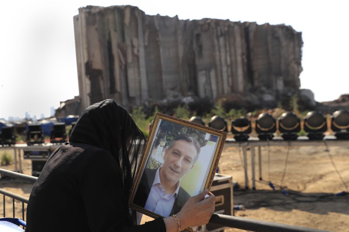 A relative of a victim who was killed in the massive blast last year at the Beirut port reacts and holds his portrait as she attends a mass held to commemorate the first year anniversary, at the Beirut port, Lebanon, Wednesday, Aug. 4, 2021. (AP Photo/Hussein Malla)