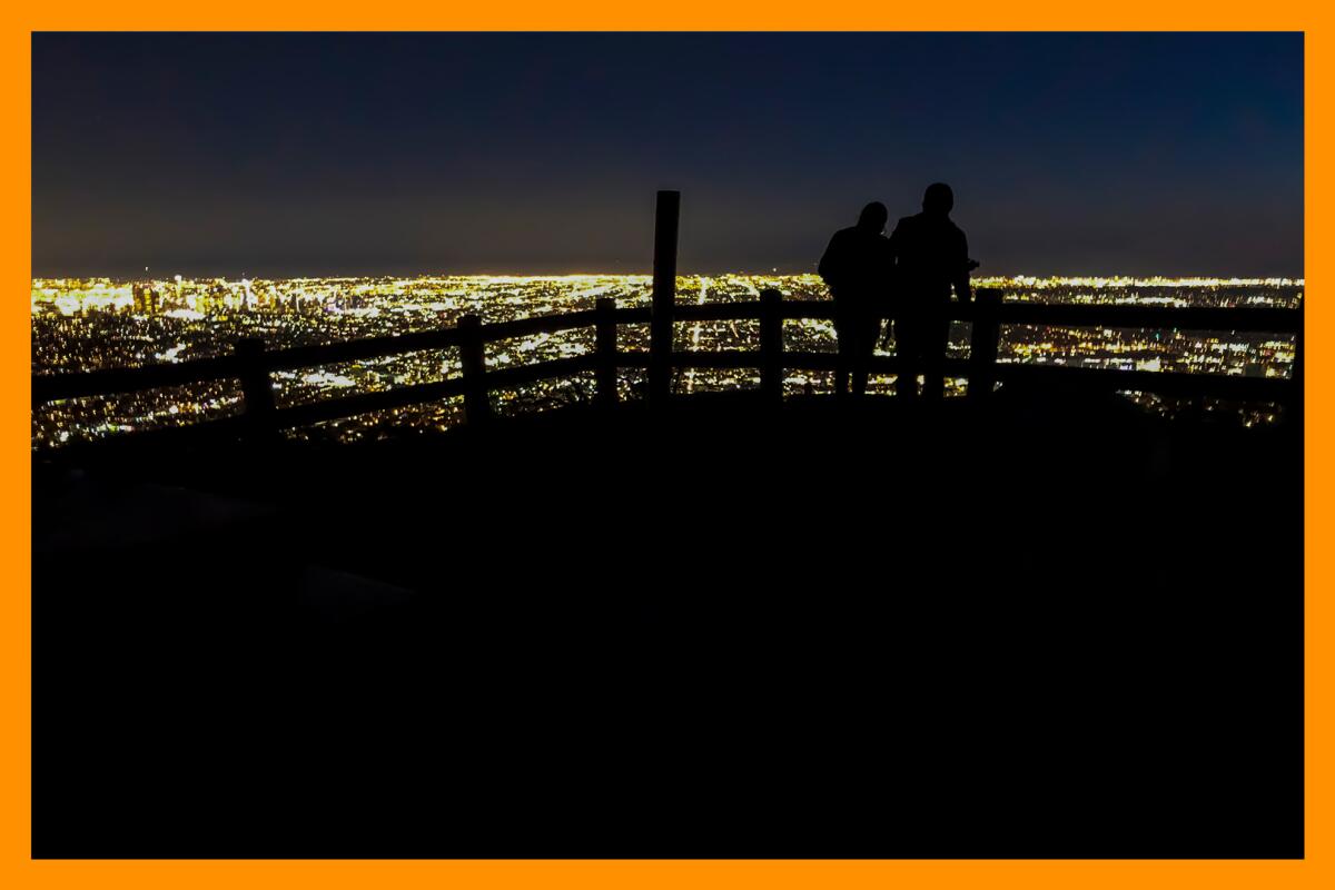Two people in silhouette against the lights of L.A. at night on Mt. Hollywood