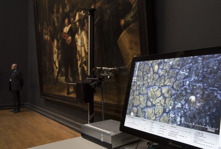 FILE - A microscopic image enlarging a 4x6 millimeter part of the painting on Rembrandt's Night Watch, which will be restored next year in the public eye, is seen on a screen next to the painting at the Rijksmuseum in Amsterdam, Netherlands, Tuesday, Oct. 16, 2018. Rembrandt van Rijn's iconic and huge painting "The Night Watch" is now also a supersized museum photo delivered right to your laptop in unsurpassed detail. The Amsterdam Rijksmuseum on Monday Jan. 3, 2022, put on its digital portal what it called "the most detailed photograph of any artwork" ready for assessment by scientists and art lovers alike. It is expected to draw widespread interest especially since the museum is closed because of coronavirus measures.(AP Photo/Peter Dejong, File)