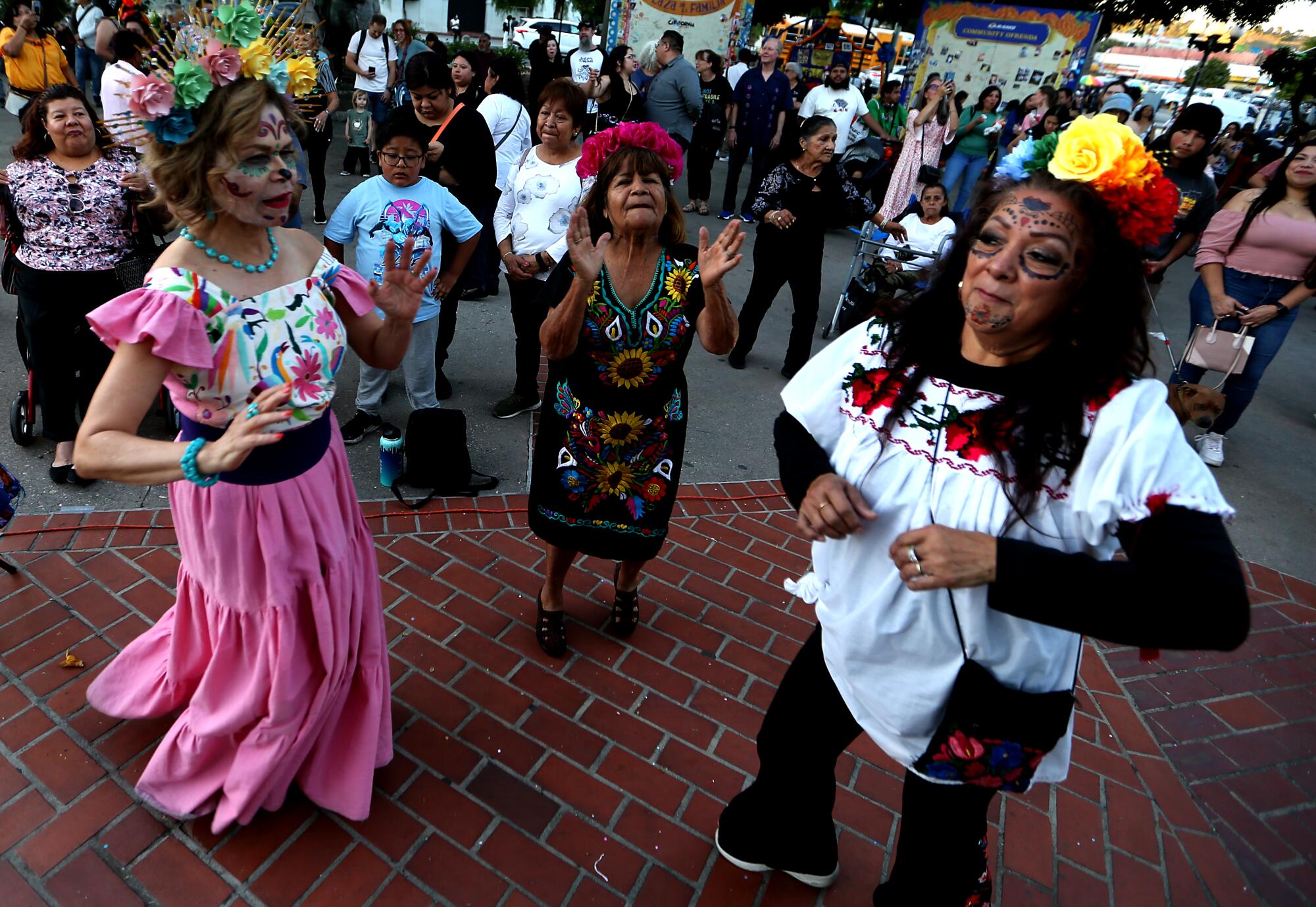 Women in costumes and face paint dance in Olvera Plaza during Day of the Dead festivities.