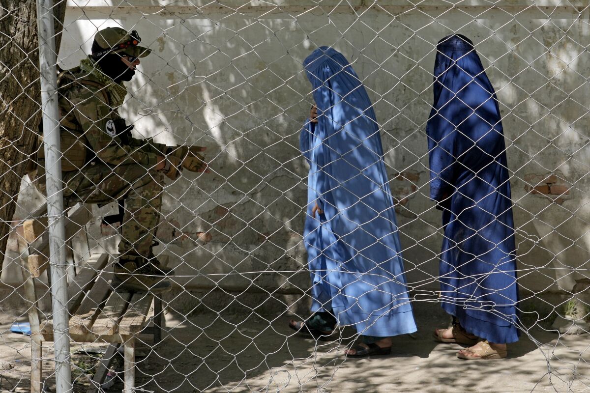 A Taliban fighter stands guard as two women enter the government passport office, in Kabul, Afghanistan, Wednesday, April 27, 2022. .Afghanistan's Taliban leadership has ordered all Afghan women to wear the all-covering burqa in public. The decree Saturday, May 7, evoked similar restrictions on women during the Taliban's previous hard-line rule between 1996 and 2001. (AP Photo/Ebrahim Noroozi)