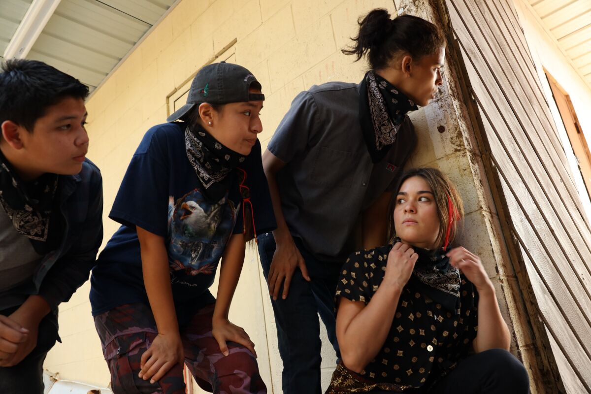 Four teens peer around the corner of a building.