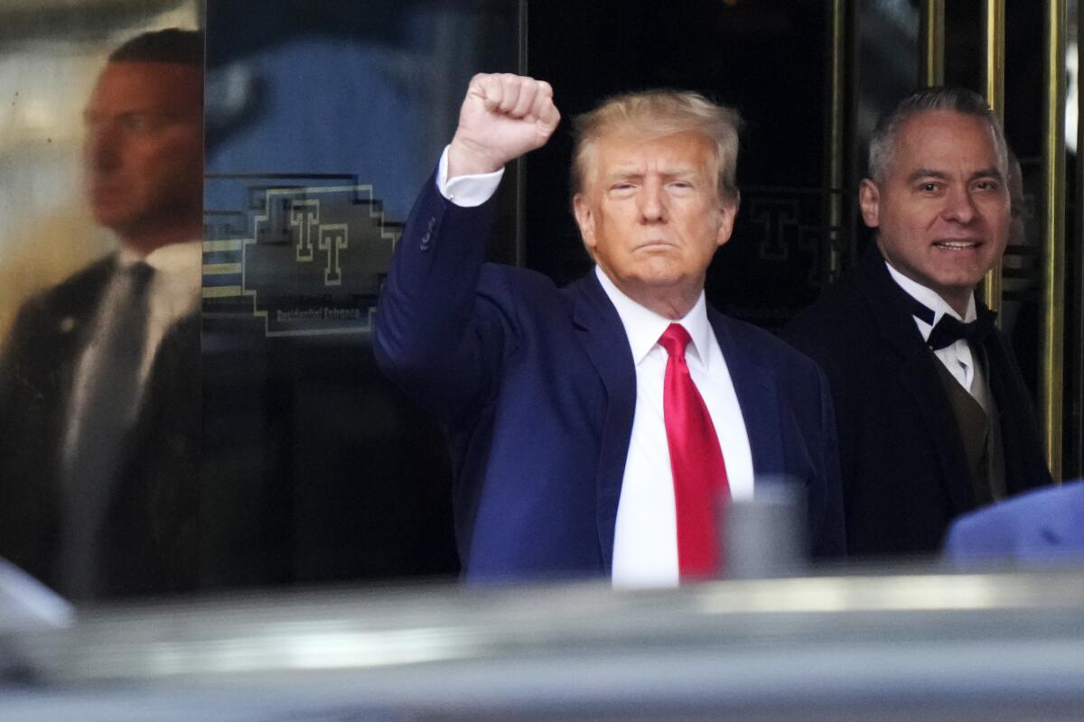 Donald Trump, wearing a dark suit and red tie, raises a fist.