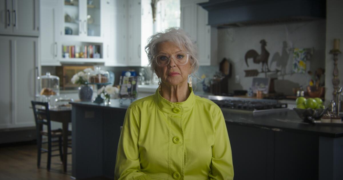 A woman in a green top sits in her kitchen alone.