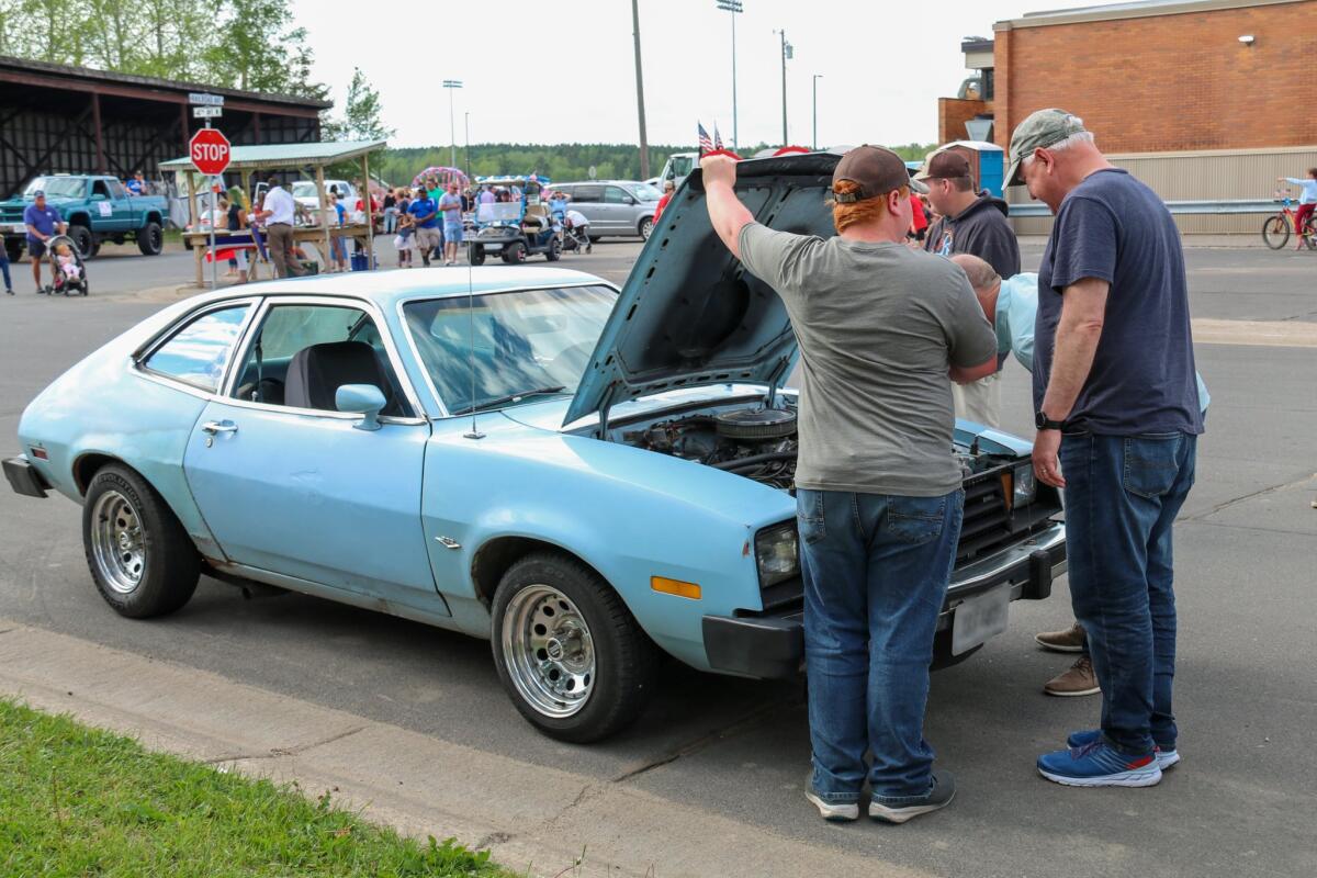 Tim Walz and others watch the engine of a light blue Ford Pinto parked on the street as a person lifts the hood.