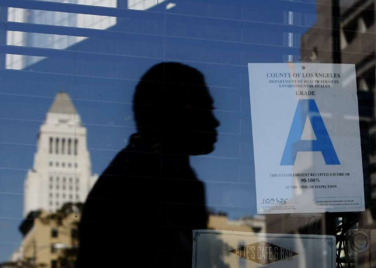 A pedestrian and Los Angeles City Hall are reflected in the window of Pete's Cafe & Bar in downtown L.A., which has an A grade rating from County Environmental Health inspectors. Starting Thursday, diners can view restaurant grades on Yelp, the popular review website.