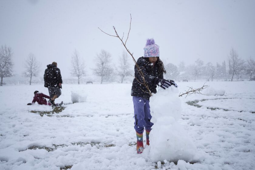 Xara Olivas makes a snowman as Timothy Olivas and Xabrina Olivas play in the snow during a storm in Acton, California, US, on Saturday, Feb. 25, 2023. (Eric Thayer/For The Times)